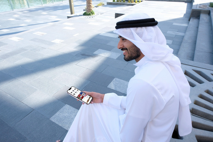 رجل كويتي يحمل هاتفه ويتصفح التطبيق.
